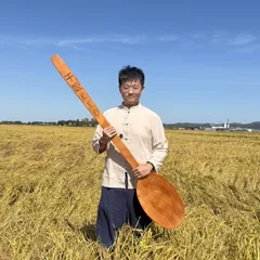 干饭CEO 在稻田里，手握刻着「干饭CEO」的大木勺
